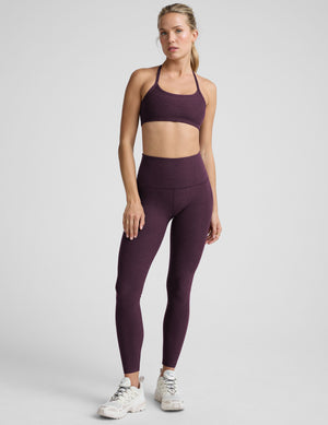 model wearing a purple slim strapped racerback bra and leggings on a light gray background. 