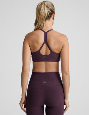 model wearing a purple slim strapped racerback bra and leggings on a light gray background. 