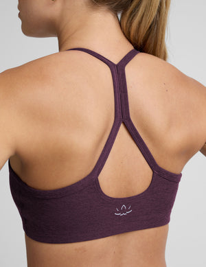 model wearing a purple slim strapped racerback bra and leggings on a light gray background. 