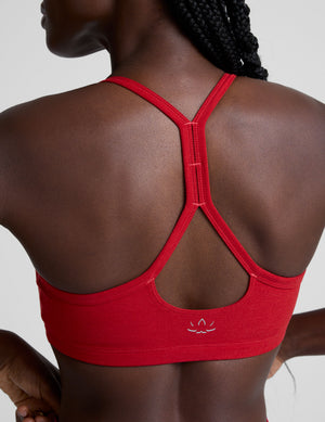 Woman wearing a red sports bra and leggings on a light background. 