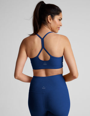 Woman wearing a blue racerback sports bra and leggings on a light gray background. 