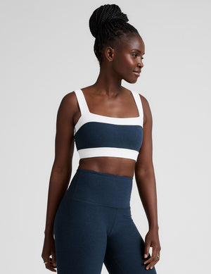 model is wearing a blue square neck bra with white horizontal colorblock stripe panels and a blue high-waisted midi length leggings. 
