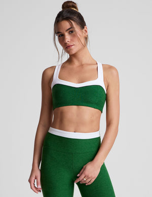 front view of green self-lined, medium to low support bra top with a colorblock sweetheart neckline panel​, contrast straps, and princess seams. bra is paired with green high-waisted midi leggings with a white contrast trim around waistband and down sides of legs. 