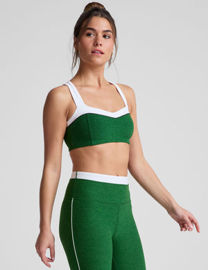 side view of green self-lined, medium to low support bra top with a colorblock sweetheart neckline panel​, contrast straps, and princess seams. bra is paired with green high-waisted midi leggings with a white contrast trim around waistband and down sides of legs. 