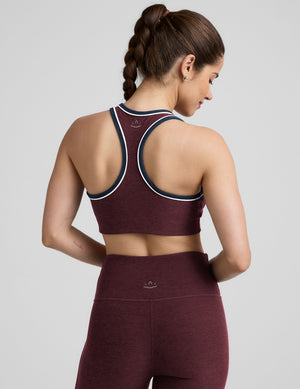 model wearing a maroon sports bra and leggings set on a gray background. 