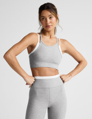 Woman wearing a gray sports bra and leggings on a light gray background. 