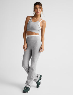 Woman wearing a gray sports bra and pants on a light gray background. 