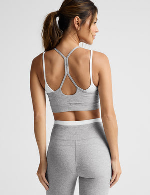 Woman wearing a gray sports bra and pants on a light gray background. 