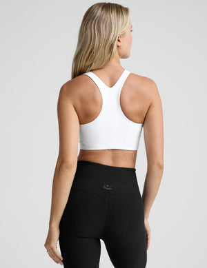 model wearing a white high-neck racerback sports bra and black leggings on a light gray background. 