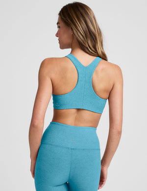 Woman wearing a blue high scoop neck racerback bra and leggings on a plain background. 