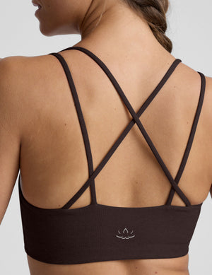 woman wearing a brown sports bra with crossover back straps and leggings on a plain background. 