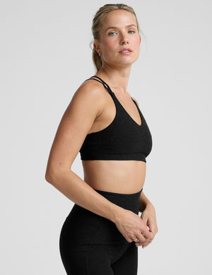 woman wearing a black sports bra with back crossover straps and leggings on a plain background. 