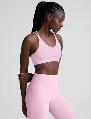 Woman wearing a pink v-neck bra with crossover back straps and leggings on a plain background. 