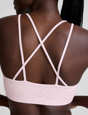 Pink sports bra with criss-cross straps worn by a person on a neutral background