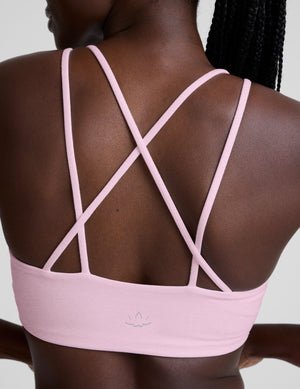 Woman wearing a pink v-neck bra with crossover back straps and leggings on a plain background. 