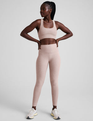 model wearing a pink scoop neck racerback long line sports bra and leggings set on a light gray background. 