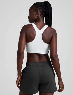 woman wearing a white sports bra and black shorts on a plain background. 