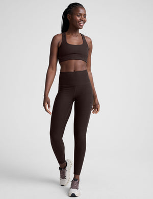 woman wearing a brown racerback bra and leggings on a plain background. 