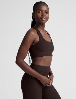 woman wearing a brown racerback bra and leggings on a plain background. 