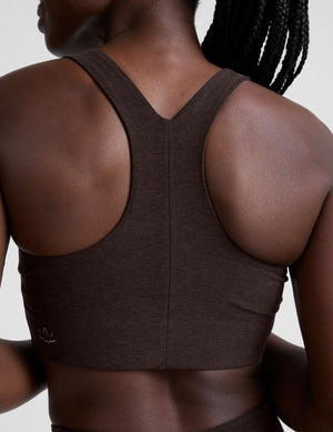 woman wearing a brown racerback bra and leggings on a plain background. 