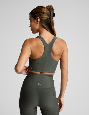 Woman wearing a green bra and leggings on a light gray background. 