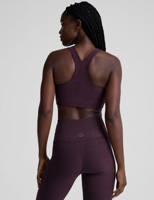 model wearing a purple scoop neck racerback long line sports bra and leggings set on a plain background. 