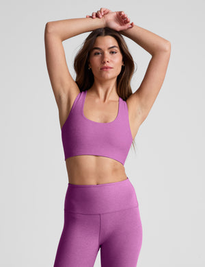 Woman wearing a purple sports bra and leggings against a plain background. 