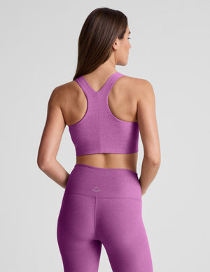 Woman wearing a purple sports bra and leggings against a plain background. 