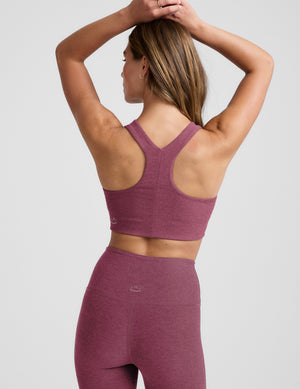 Woman wearing a purple sports bra and leggings on a light gray background. 