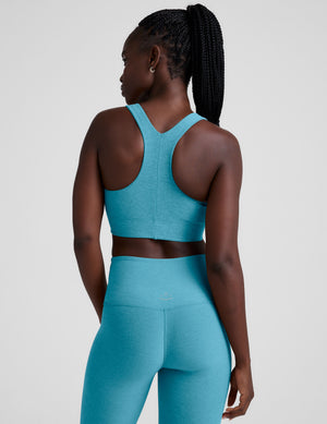 Woman wearing a blue long line racerback sports bra and leggings on a plain background. 