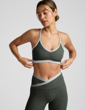 Woman wearing a green sports bra and leggings on a light gray background. 