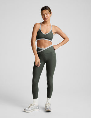 Woman wearing a green sports bra and leggings set on a light gray background. 