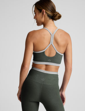 Woman wearing a green sports bra and leggings on a light gray background. 