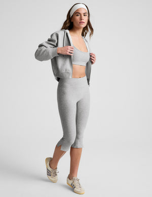 Woman wearing gray bra and pedal pushers against a plain background. 