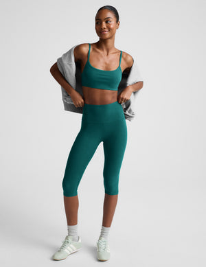 Woman wearing a green sports bra and leggings against a plain background. 