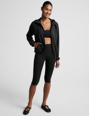 Woman wearing a black jacket and black leggings on a white background. 