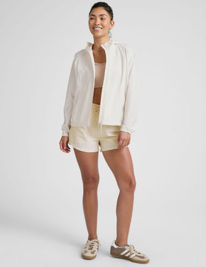 model wearing a white jacket and shorts on a plain background. 