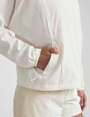 model wearing a white zip-up jacket with hood and shorts on a plain background. 