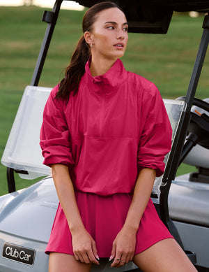 Woman in a red half zip jacket and skirt sitting on the hood of a golf cart. 