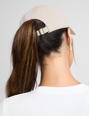 A woman wearing a beige baseball cap with 'CLUB BEYOND' embroidered in white on the front, paired with a white long-sleeve top against a light gray background.