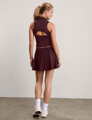 A woman wearing a sleeveless high-neck athletic top and matching mini skirt in a deep burgundy color, shown from the back against a neutral studio background.