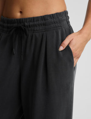 Close-up of a person wearing dark charcoal gray lounge pants with an elastic drawstring waistband and side pockets, with one hand in the pocket.