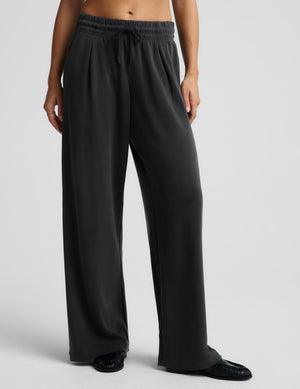 A woman modeling a matching dark gray lounge set consisting of a quarter-zip long-sleeve top and wide-leg sweatpants, photographed against a solid light gray studio background.