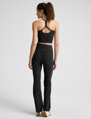 Woman wearing a black racerback cropped tank and black pants against a plain background. 