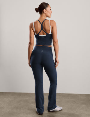 A woman modeling a matching athletic set consisting of a dark navy cropped tank with white trim and high-waisted dark navy blue bootcut pants, standing against a neutral studio backdrop.