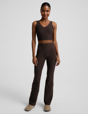 Woman wearing a brown cropped tank top and brown high-waisted bootcut pants against a plain background. 