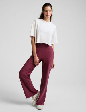 A woman modeling a white cropped short-sleeve t-shirt and high-waisted, wide-leg burgundy pants against a light gray studio background.