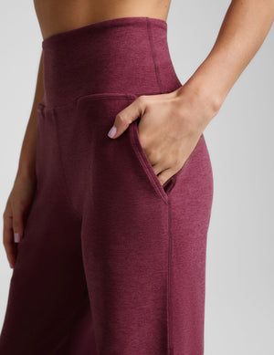 Close-up of a model wearing heathered burgundy high-waisted lounge pants with side pockets, showing the waistband and hand in the pocket against a light gray background.