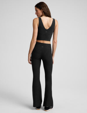 Woman wearing a black cropped tank and black mid-rise bootcut pants against a plain background. 