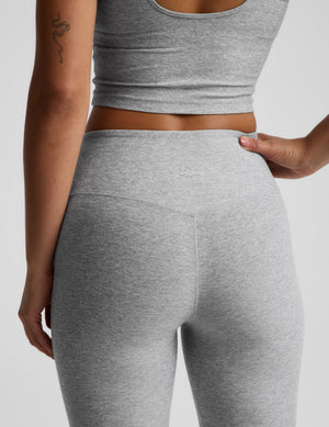 Woman wearing a gray racerback cropped tank top and mid rise bootcut pants against a plain background. 